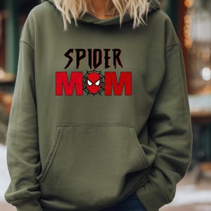 May include: A green hooded sweatshirt with the text "SPIDER MOM" in black and red lettering. A red spider-man face is in the center of the text.
