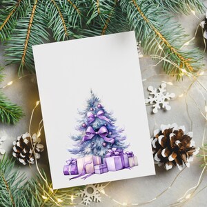 Puede incluir: Una tarjeta blanca con una ilustraci&oacute;n de acuarela de un &aacute;rbol de Navidad azul decorado con lazos y adornos morados. El &aacute;rbol est&aacute; rodeado de cajas de regalo moradas con lazos blancos. La tarjeta est&aacute; rodeada de ramas de pino, copos de nieve blancos y una cadena de luces blancas.