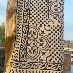 May include: A beige cotton fabric with a black and white block print design. The fabric features a geometric pattern with dots, zigzags, and floral motifs.