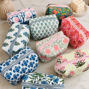May include: A collection of eight rectangular quilted fabric pouches featuring various block-printed floral and botanical patterns in colors including blue, pink, green, and orange. Each pouch has a zippered closure with a striped fabric trim.
