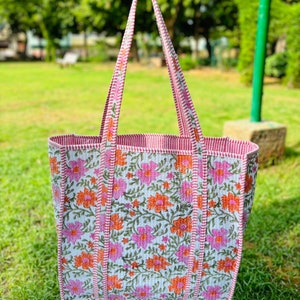 May include: A white tote bag with pink and orange floral print. The bag has red and white striped straps and a red and white striped trim.