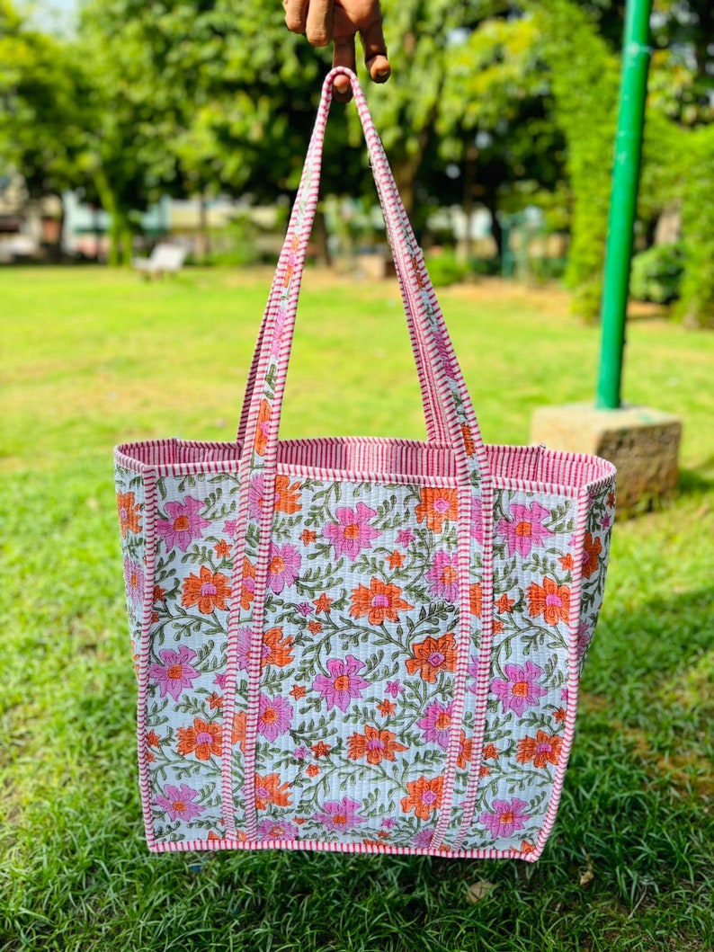 May include: A white tote bag with pink and orange floral print. The bag has red and white striped straps and a red and white striped trim.