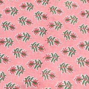 Puede incluir: Primer plano de una tela rosa con un estampado floral repetitivo. El patr&oacute;n presenta hojas verdes y flores rojas con centros verdes. El dise&ntilde;o est&aacute; espaciado uniformemente sobre la tela, creando un textil visualmente atractivo.
