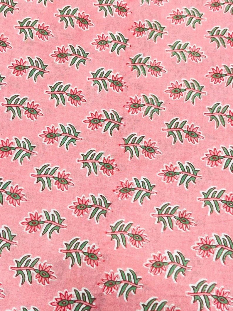 Puede incluir: Primer plano de una tela rosa con un estampado floral repetitivo. El patr&oacute;n presenta hojas verdes y flores rojas con centros verdes. El dise&ntilde;o est&aacute; espaciado uniformemente sobre la tela, creando un textil visualmente atractivo.