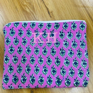 Op de afbeelding: Een roze gewatteerde etui met een herhalend bloemmotief in groen en marineblauw. De etui heeft een witte rits en de initialen "KH" in een lichtere roze kleur. De etui is rechthoekig en lijkt van stof te zijn.