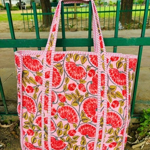 May include: A pink tote bag with a floral print. The bag has white and red stripes around the edges and a pink and white striped handle.