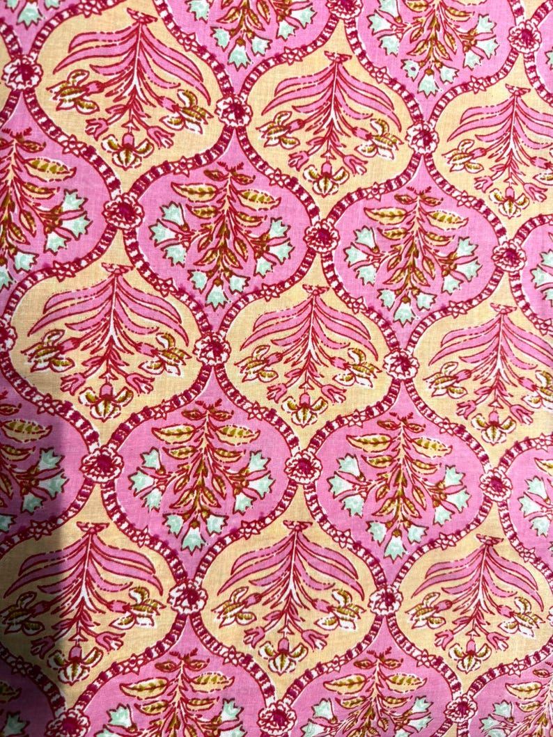 Op de afbeelding: Close-up van een stof met een herhalend bloemenpatroon. Het ontwerp heeft roze, lichtroze en bruine kleuren. De bloemelementen zijn gestileerd met een mix van gebogen lijnen en gedetailleerde vormen, waardoor een visueel rijke textiel ontstaat.