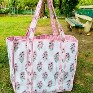 May include: A white and pink quilted tote bag with floral print and pink and white striped handles.