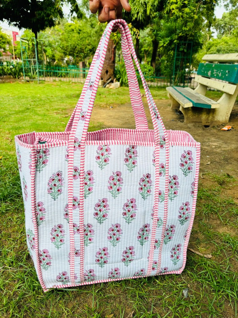 May include: A white and pink quilted tote bag with floral print and pink and white striped handles.
