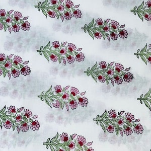 Op de afbeelding: Witte stof met een herhaald patroon van bloemboeketten. Elk boeket heeft roze bloemen met rode centra en groene bladeren. Het ontwerp is gelijkmatig verdeeld over de stof.