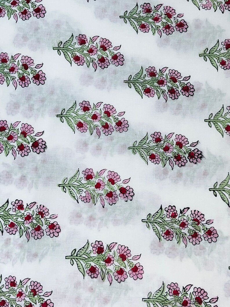 Op de afbeelding: Witte stof met een herhaald patroon van bloemboeketten. Elk boeket heeft roze bloemen met rode centra en groene bladeren. Het ontwerp is gelijkmatig verdeeld over de stof.
