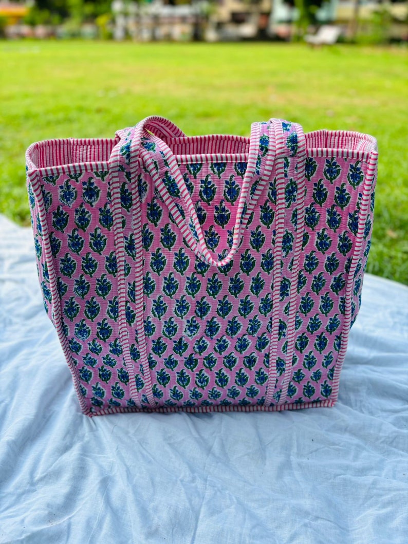 May include: A pink and white striped tote bag with a floral pattern. The bag has two handles and is made of a sturdy fabric.