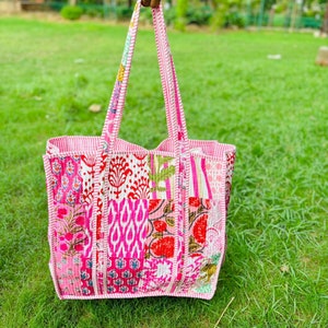 Könnte beinhalten: Eine rosafarbene Patchwork-Tragetasche mit weißen Verzierungen und floralen Mustern. Die Tasche hat zwei Henkel und ist aus Baumwollstoff gefertigt.