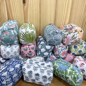 以下が含まれることがあります： 青、緑、ピンク、白などの色合いで、様々な花や植物のブロックプリント柄が施された、小さな長方形のキルティング生地のポーチのコレクション。各ポーチにはファスナーが付いており、柔らかく質感のある表面が特徴です。