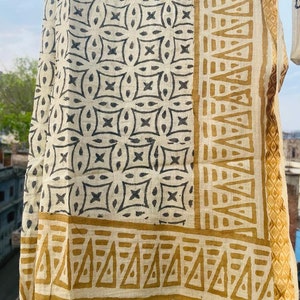 May include: A white cotton scarf with a black and brown geometric pattern. The scarf has a border of brown triangles.