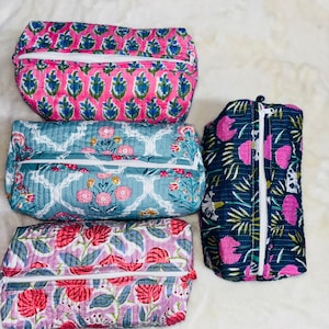 Könnte beinhalten: Vier gesteppte Kosmetiktaschen mit floralen Mustern. Die Taschen haben eine rechteckige Form mit Reißverschluss. Die Muster umfassen rosa und blaue Blumenmuster auf rosa Hintergrund, ein blaues Blumenmuster auf blauem Hintergrund und ein rosa Blumenmuster auf lila Hintergrund.