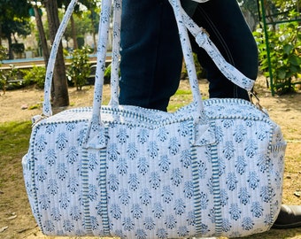 May include: A white and blue patterned cotton duffel bag with a long strap. The bag has a quilted design and is made of a soft, durable fabric.
