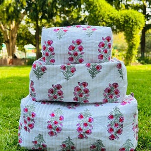 May include: Three white fabric storage boxes with a pink floral print. The boxes are stacked on top of each other.