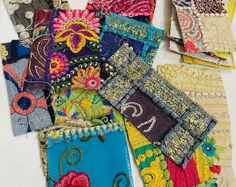 May include: Assortment of colorful fabric scraps with intricate embroidery and patchwork designs. The fabrics are in various shades of blue, green, pink, yellow, and red. Some of the fabrics have floral patterns, while others have geometric designs.