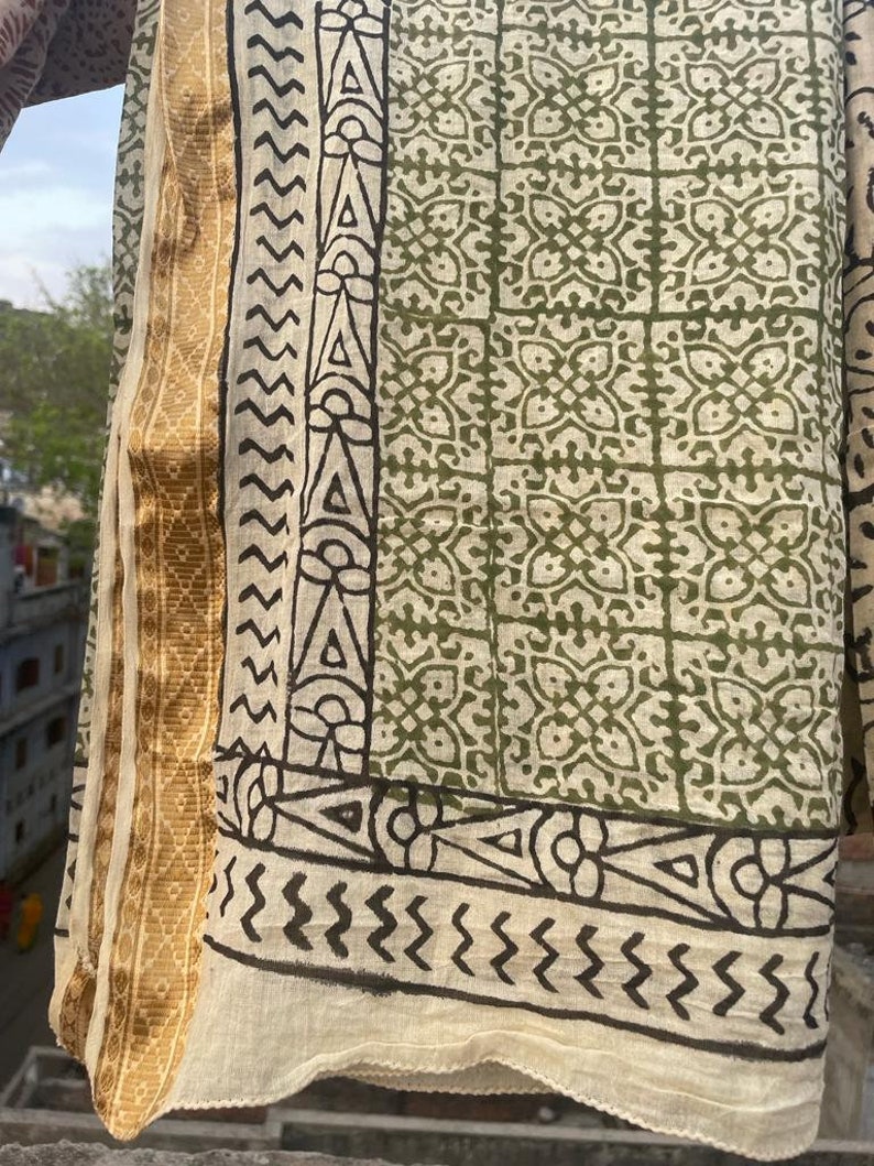 May include: A cream-colored cotton fabric with a green and black block print design. The fabric has a gold border.