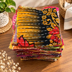 Puede incluir: Una pila de parches de tela cuadrados con una variedad de colores y patrones vibrantes, que incluyen negro, amarillo, rojo y motivos florales. Cada pieza está unida con costuras blancas visibles en un estilo tradicional kantha.