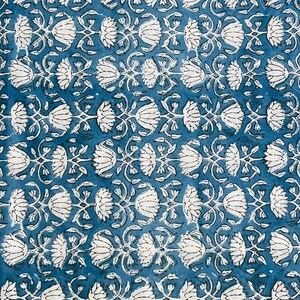Op de afbeelding: Een close-up van een blauw en wit bloemenpatroon. Het ontwerp toont witte bloemen en bladeren gerangschikt in rijen tegen een blauwe achtergrond. Het patroon herhaalt zich over de stof en cre&euml;ert een visueel aantrekkelijk textiel.