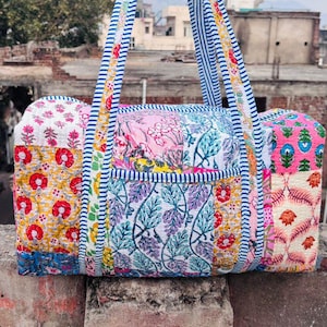 Könnte beinhalten: Eine Patchwork-Duffel-Tasche mit blau-weiß gestreiften Trägern. Die Tasche ist aus Baumwollstoff mit verschiedenen Blumendrucken in Rosa, Gelb, Blau und Rot.