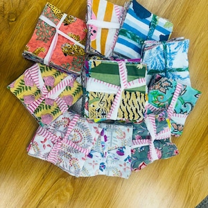 Peut inclure: Une collection de serviettes en tissu carrées attachées avec des liens en tissu blanc, présentant divers motifs colorés incluant des imprimés léopard, des motifs floraux, des rayures et des illustrations botaniques en rose, jaune, bleu, vert et orange.