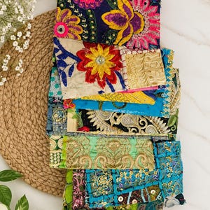 May include: A stack of rectangular fabric pieces featuring vibrant, multi-colored patchwork designs. The textiles display intricate embroidery, floral motifs, metallic gold thread accents, sequins, and varied patterns in shades of blue, green, yellow, and pink.