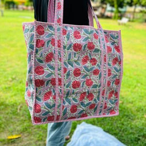 May include: A large tote bag with pink and green floral print. The bag has pink and white striped straps.