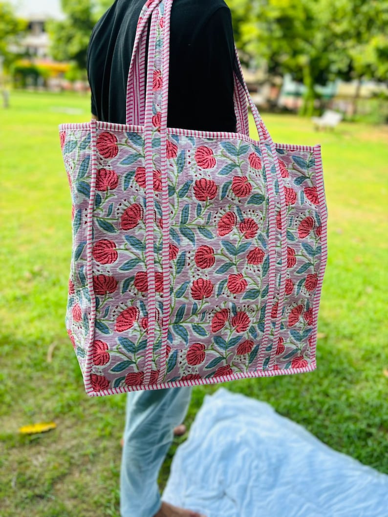 May include: A large tote bag with pink and green floral print. The bag has pink and white striped straps.