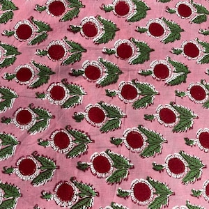 Puede incluir: Tela rosa con un patr&oacute;n repetido de flores rojas y blancas con hojas verdes. Las flores tienen un c&iacute;rculo central rojo rodeado de p&eacute;talos blancos. Las hojas son verdes. La tela tiene un aspecto suave y ligeramente arrugado.