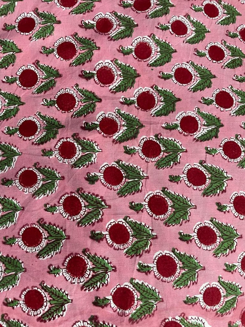 Puede incluir: Tela rosa con un patr&oacute;n repetido de flores rojas y blancas con hojas verdes. Las flores tienen un c&iacute;rculo central rojo rodeado de p&eacute;talos blancos. Las hojas son verdes. La tela tiene un aspecto suave y ligeramente arrugado.