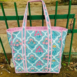 May include: A blue and pink floral tote bag with white trim. The bag has a quilted design and is made of cotton.
