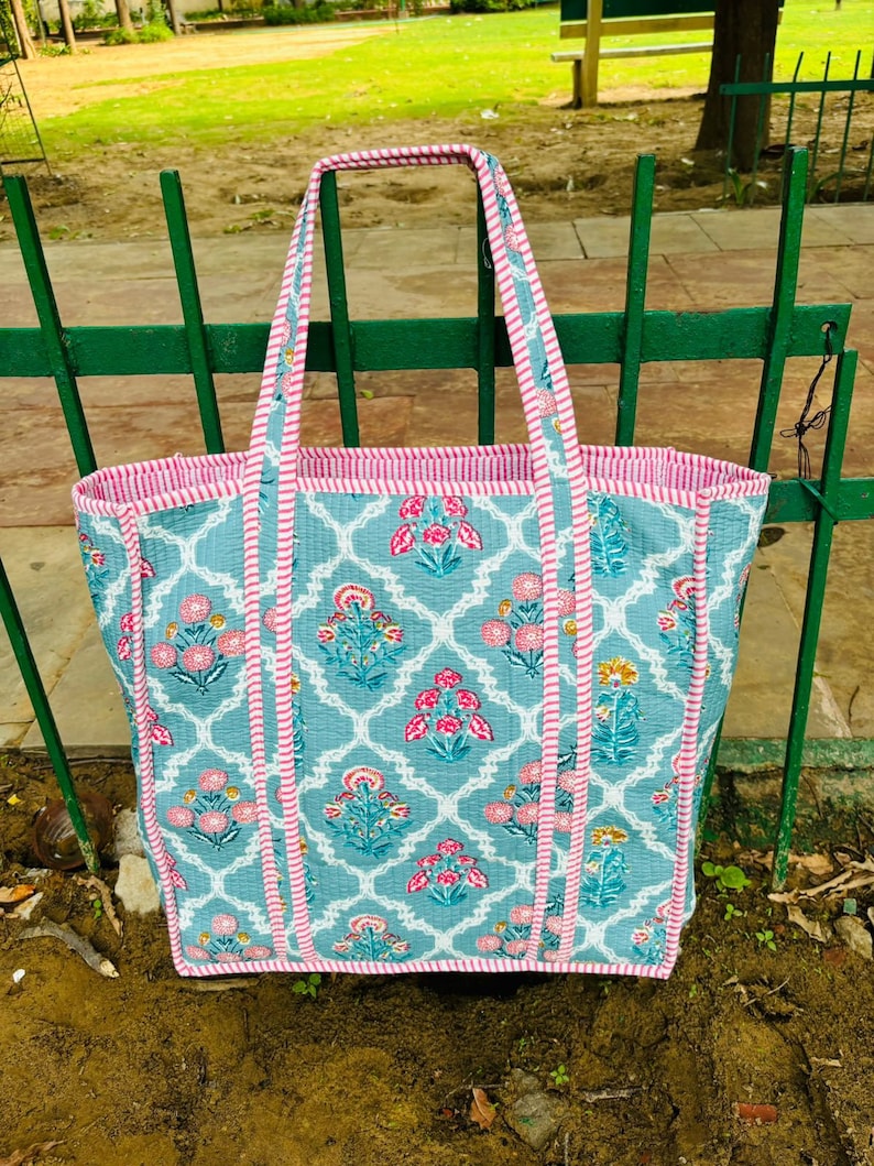 May include: A blue and pink floral tote bag with white trim. The bag has a quilted design and is made of cotton.