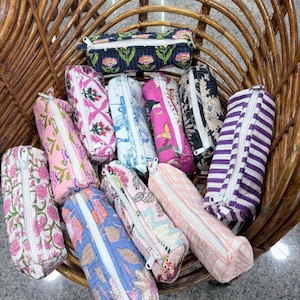 Könnte beinhalten: Eine Sammlung von zehn rechteckigen Stiftemäppchen aus Stoff mit weißen Reißverschlüssen, die verschiedene Muster wie Blumenprints, Streifen und geometrische Designs in Farben wie Rosa, Blau, Lila, Schwarz und Orange aufweisen und in einem Korb liegen.