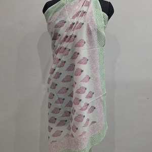 May include: A white sarong featuring a repeating pattern of small pink leaf-like motifs. The fabric is bordered by a light green chevron pattern and a thin band of pink floral detailing. The garment is draped over a black mannequin torso.