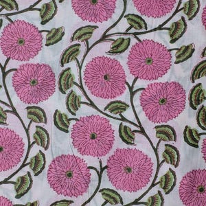 Op de afbeelding: Een herhalend bloemenpatroon met grote roze bloemen met gedetailleerde centra en groene bladeren. De bloemen en bladeren zijn verbonden door donkerbruine stelen, tegen een witte achtergrond. Close-up van een stof.