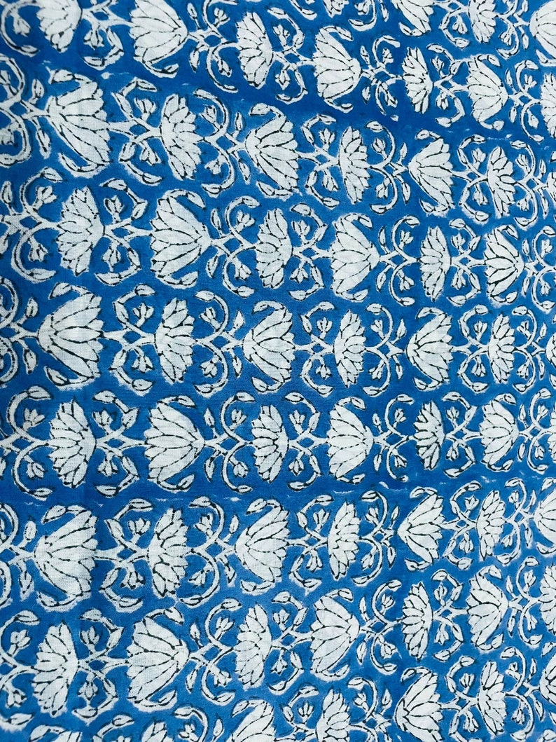 Puede incluir: Primer plano de un patr&oacute;n floral azul y blanco. El dise&ntilde;o presenta motivos repetidos de flores y hojas blancas sobre un fondo azul vibrante. La tela tiene una apariencia texturizada, lo que sugiere una fibra natural.