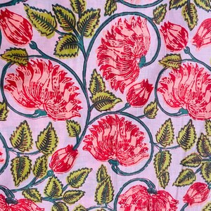Puede incluir: Primer plano de una tela con estampado floral. Grandes flores rojas con p&eacute;talos detallados se intercalan con hojas y capullos verdes sobre un fondo rosa claro. El dise&ntilde;o presenta un patr&oacute;n repetitivo de flores y follaje estilizados.