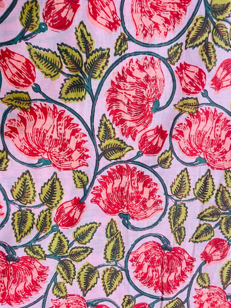 Puede incluir: Primer plano de una tela con estampado floral. Grandes flores rojas con p&eacute;talos detallados se intercalan con hojas y capullos verdes sobre un fondo rosa claro. El dise&ntilde;o presenta un patr&oacute;n repetitivo de flores y follaje estilizados.