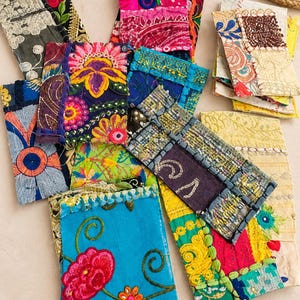 May include: A collection of rectangular fabric pouches featuring vibrant patchwork designs with intricate embroidery, floral motifs, and varied textures in bright colors including turquoise, magenta, yellow, and deep blue, arranged in a scattered layout.