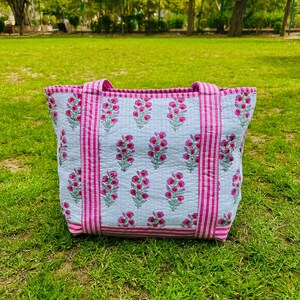 May include: A white tote bag with pink and white stripes and a floral print. The bag has two handles.