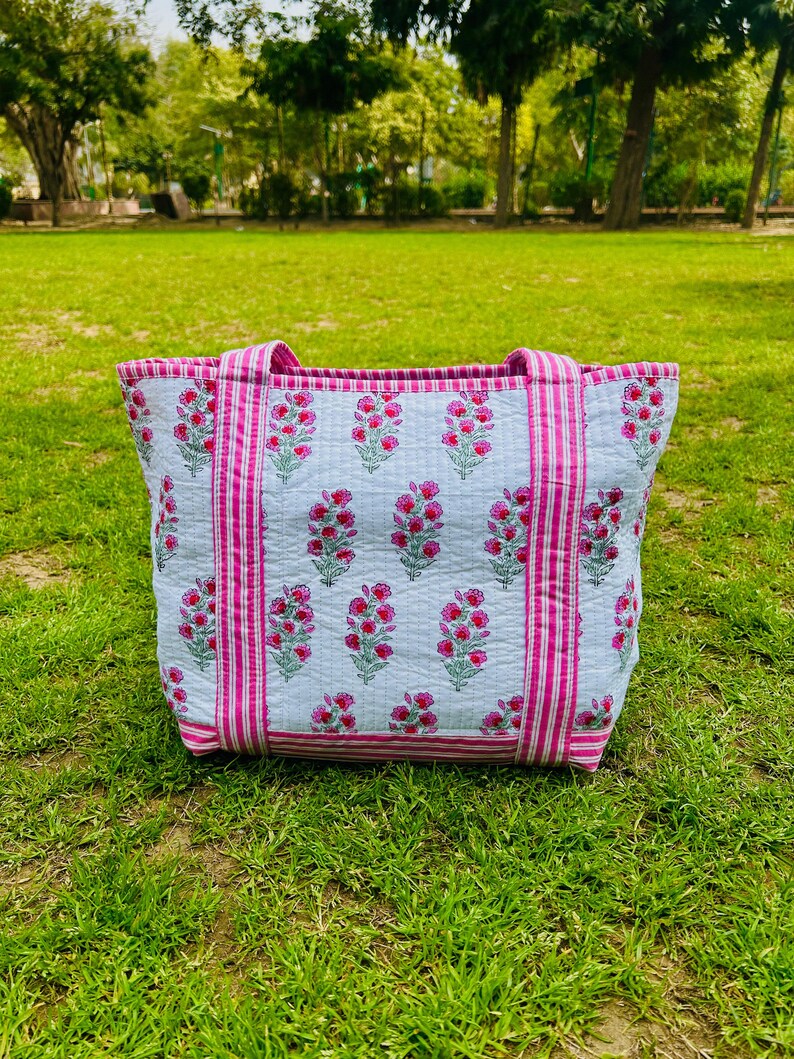 May include: A white tote bag with pink and white stripes and a floral print. The bag has two handles.