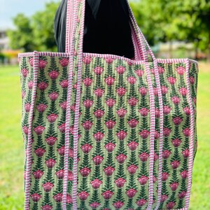 May include: A large green and pink floral tote bag with white stripes on the handles. The bag has a quilted design and is made of cotton.