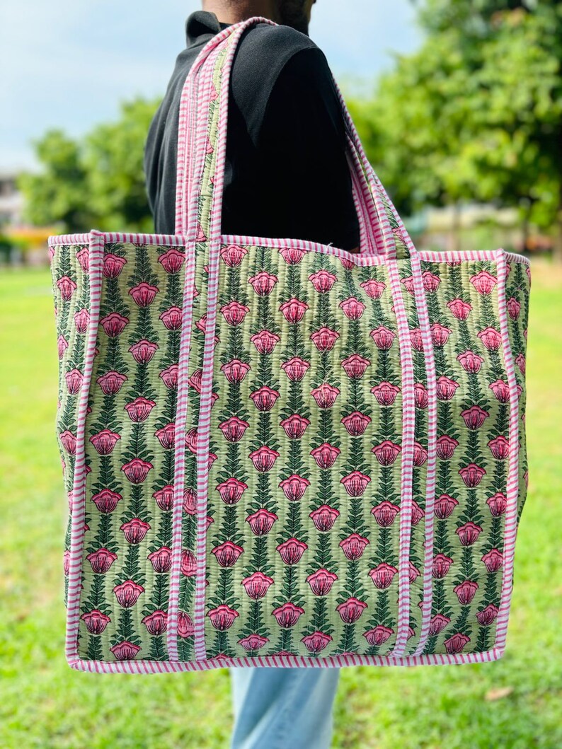 May include: A large green and pink floral tote bag with white stripes on the handles. The bag has a quilted design and is made of cotton.