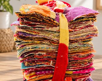 May include: A tall, vertical stack of assorted fabric squares featuring a variety of vibrant colors including purple, orange, red, and yellow. The fabric pieces are held together by a single, long, knotted strip of yellow and red fabric.