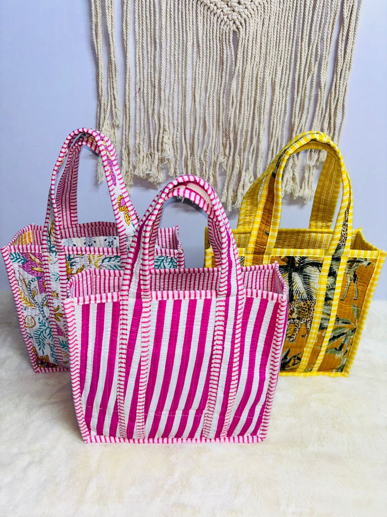 Puede incluir: Tres bolsos tote coloridos con asas resistentes. Un bolso presenta rayas verticales rosas y blancas, otro tiene un estampado de animales amarillo y marr&oacute;n, y el tercero tiene un estampado floral. Los bolsos est&aacute;n hechos de tela acolchada.