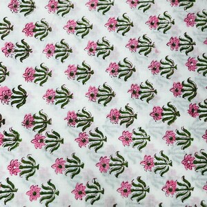 May include: White fabric with a repeating pattern of pink flowers and green leaves. The flowers are stylized and have a simple design.