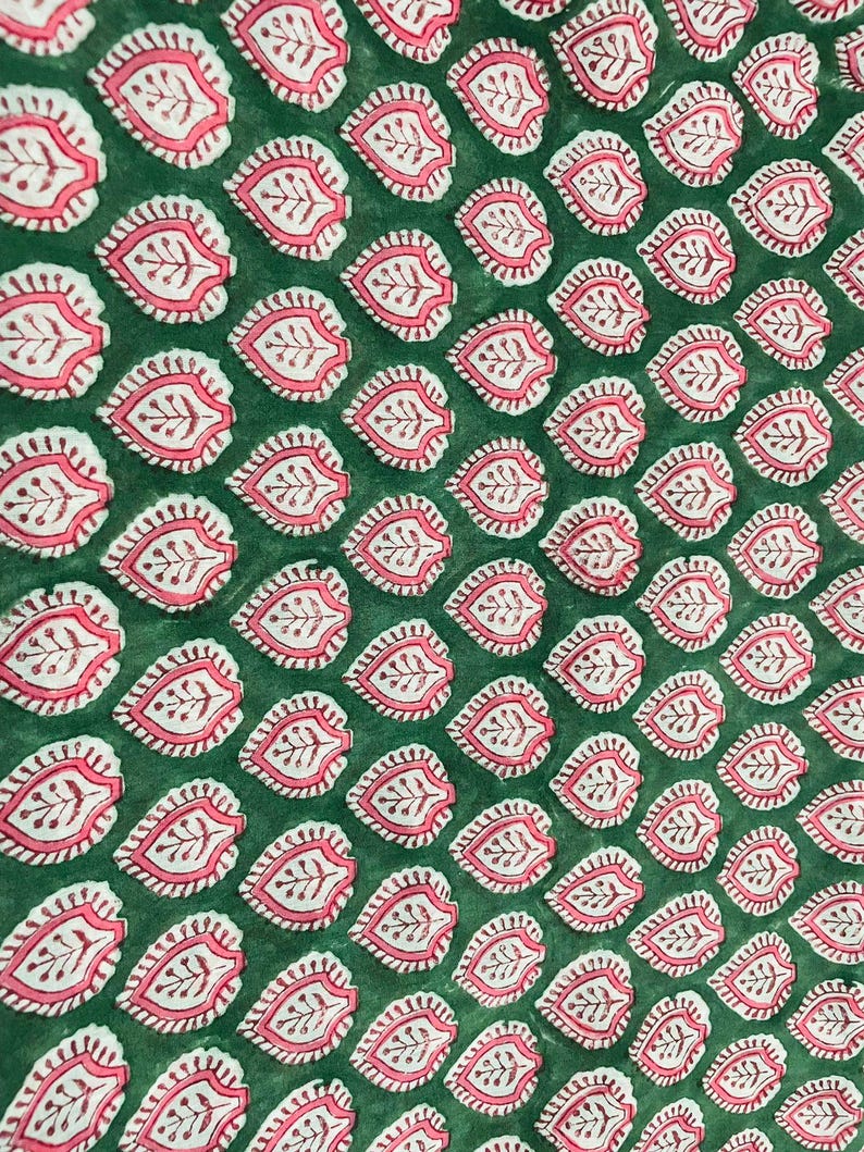 Op de afbeelding: Close-up van een groene stof met een herhaald patroon van roze en witte bladachtige ontwerpen. De bladeren hebben een gedetailleerd, aderachtig patroon aan de binnenkant. De stof heeft een licht getextureerd uiterlijk.